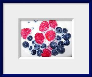 A bowl of fresh red raspberries and blueberries splashed with milk makes a healthy breakfast still life.