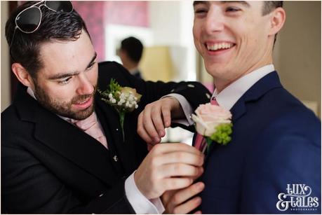 Groom preparation photography East Riddlesden Hall Wedding Photographer help groomsman with pink rose buttonhole