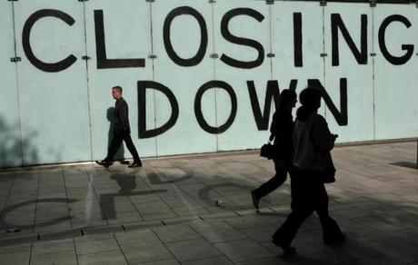 Shoppers walk past a closing down sign in a shop window in Cardiff, Wales