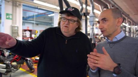This image provided by Dog Eat Dog Films shows director Michael Moore, left, and Claudio Domenicali, CEO of Ducati, in a scene from his documentary, 