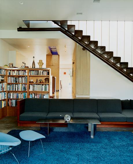 A built-in sofa with Design Tex upholstery marks the boundary between the two-level addition and the bungalow. Leading up to the master bedroom, a perforated metal staircase, lit from above, casts a Sigmar Polke–like shadow grid on the concrete floor.