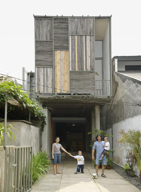 The family poses in the driveway out front of the house. The sliding panels on the facade allow a peek into the balcony just inside.