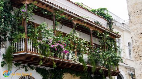 Intricate wooden balcony covered in flowers above a Cartagena street.