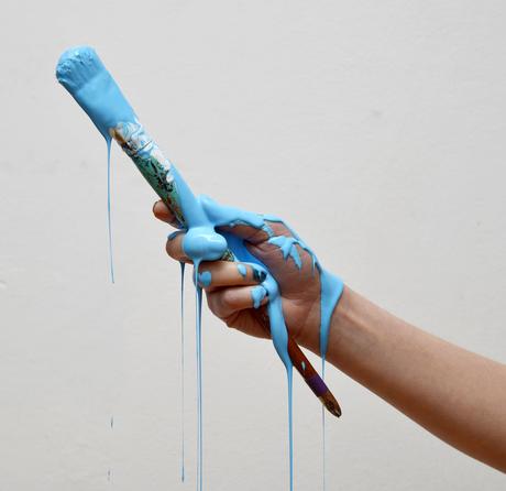 A hand holding a paintbrush covered in blue paint dripping everywhere