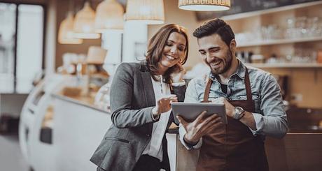 4 Ways Neighborhood Businesses Can Finally Conquer Social Media Shot of a smiling cafe owner and employee barista standing inside a coffee shop looking at new menu on a digital tablet