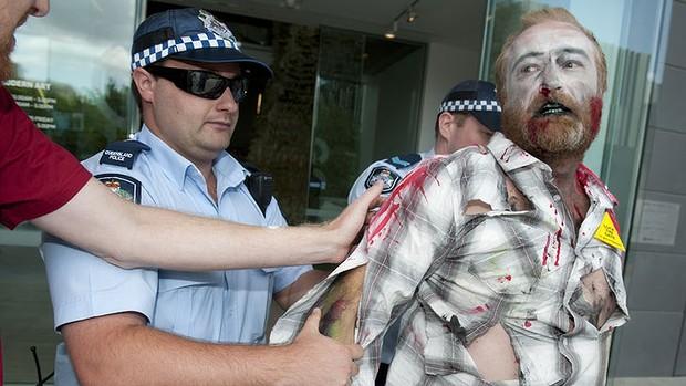Your sort not wanted . . . a ‘‘zombie farmer’’ protester is escorted by police from the Gallery of Modern Art.