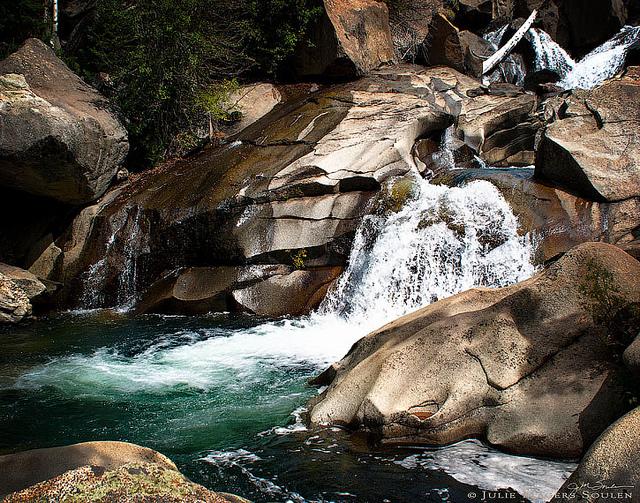 Colorado Rocky Mountain waterfall cascades over boulders and rocks into an aqua blue pool