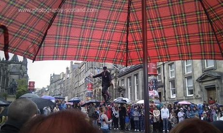 Photo - watching from under a tartan umbrella, as a unicyclist performs to the crowd at the Edinburgh Fringe, 