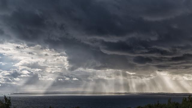 sun rays behind dark cloud ocean