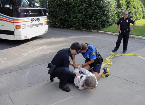 A local organizer with Katuah Earth First! is thrown to the ground and arrested in front of the bus.