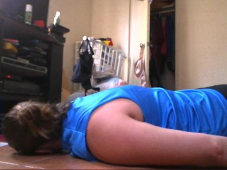 Side view of woman lying on floor, head turned away from camera, arms by her sides. There is also clothing visible in the background.