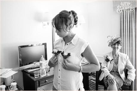 Candid photograph of bride making a funny pose with buttonhole flowers in UK hotel room 