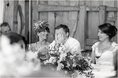 Funny wedding photograph of groom covering his face during wedding speeches at UK barn wedding 