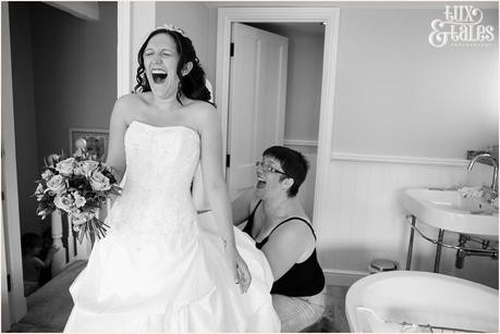 Birde and mother laugh as she is helped into wedding dress