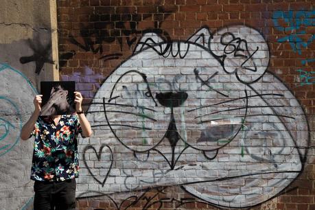 holding kirin j callinan album embracism in front of graffiti cat  