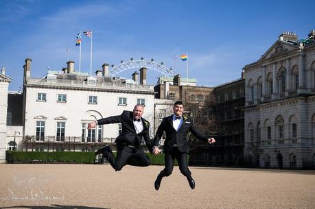 Gay couple jumping in front of gay pride flag