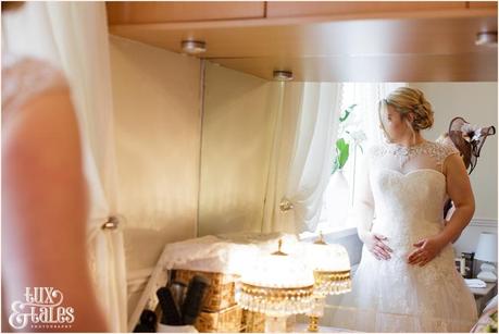 bride looks out window as her dress is fastened at yorkshire wedding