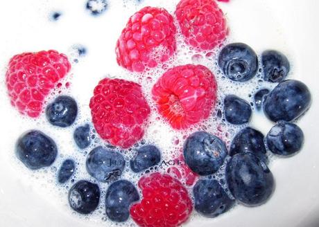 A bowl of fresh red raspberries and blueberries splashed with milk makes a healthy breakfast still life.