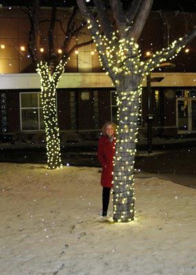 Julie in red coat behind tree with mini lights.