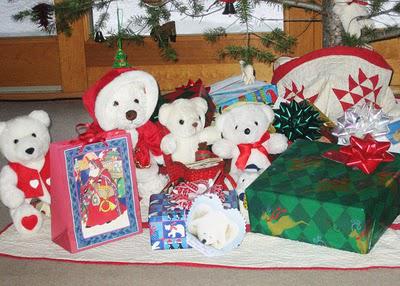 A family of white plush Christmas bears lives under a holiday tree.