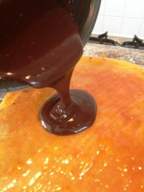 pouring dark chocolate glaze onto jam covered cake