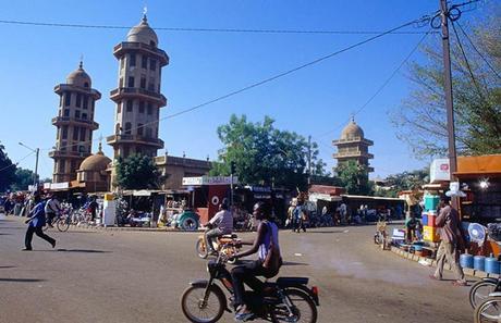 A cyclist putters past market stalls in the bustling Burkina Faso capital Ougadougou, under a bright blue sky.