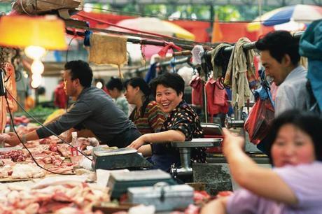 A market seller in Shanghai smiles broadly as stallholders around her serve raw meat and clothing to customers.