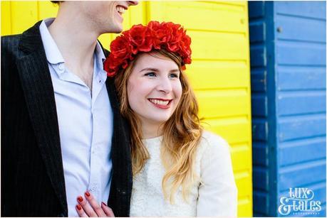 Photography Engagement Shoot in Whitby | Girl wearing Red Flower crown | Alterntive Couple whereing Vintage clothing | Hugging in front of the rainbow coloured bach huts