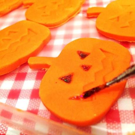 painting fondant orange pumpkin faces with edible glitter for halloween baking