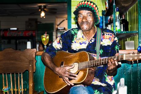 Dark skinned man in Rasta headwear holds a guitar and smiles at the camera. This is live entertainment, Bocas Town style at The Lemongrass.