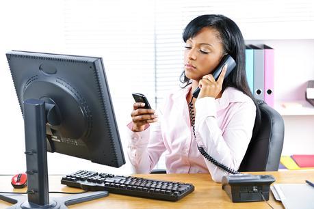 Black Businesswoman Using Two Phones At Desk