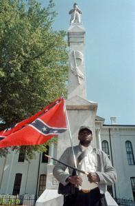 FILE - In this May 8, 2000, file photograph, Anthony Hervey holds a Confederate flag while standing underneath the Confederate monument in Oxford, Miss. (Bruce Newman/The Oxford Eagle via AP, File)