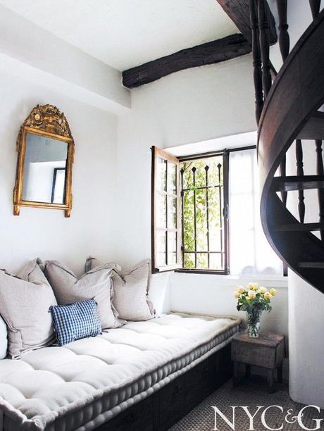 Linen tufted daybed with golden accent mirror and wood spiral staircase