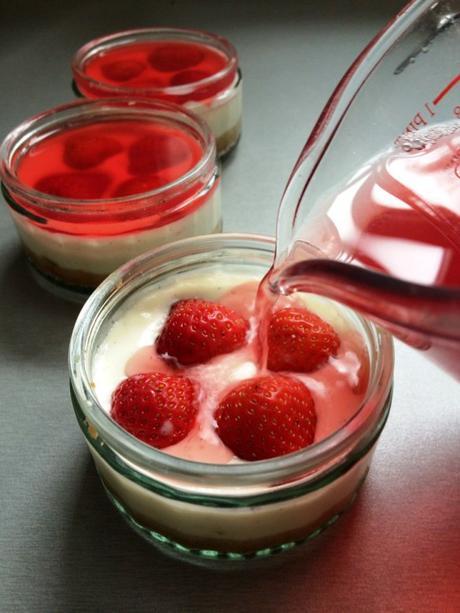 action shot pouring jelly topping onto strawberry cheesecake individual pots no bake recipe