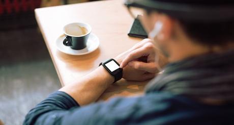 Young stylish and fashionable man checking his smartwatch in cafe bar. High angle shot. Selective focus. Toned image.