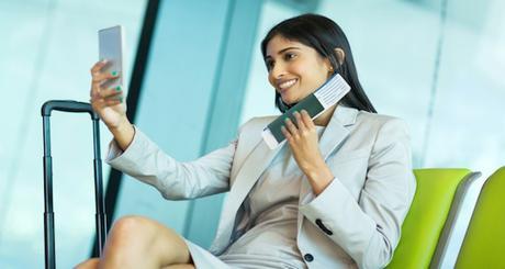 happy young business traveller taking selfie with smart phone while waiting for her flight at airport