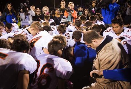 Bremerton coach Joe Kennedy, center, in blue, covers his eyes as he kneels and prays, surrounded by Centralia players, at Bremerton Memorial Stadium after the game on Friday, Oct. 16, 2015. Kennedy plans to continue his 7-year tradition of kneeling to pray at the 50-yard line after the game, disobeying district orders/Seattle Times Photo