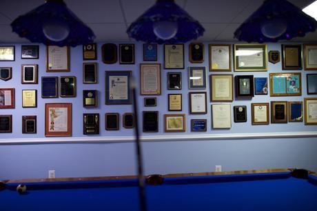 A wall covered with plaques, awards & testimonials to you-know-who in basement near a pool table