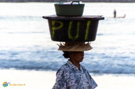 A woman sells food from the bin she carries on her head.