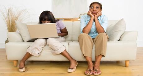 Daughter using laptop computer with unhappy mother sitting alongside