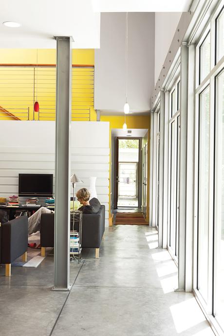 Susan relaxes on an Ikea sofa. The yellow accent wall and high ceilings enhance the lightness of the room.