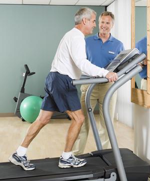 Man on treadmill with healthcare provider standing next to treadmill, supervising man's exercise.