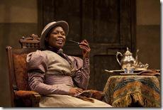 Prudence (Zainab Jah) enjoying a pipe and cup of tea at Chilford’s house in the world-premiere co-production of The Convert by Danai Gurira, directed by Emily Mann.