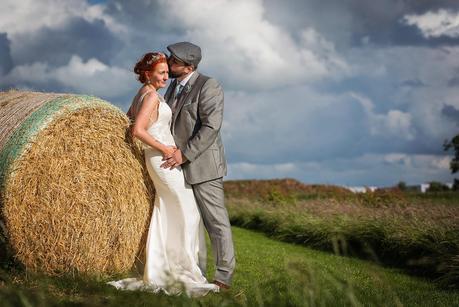 groom kissing brides head against hay bails 