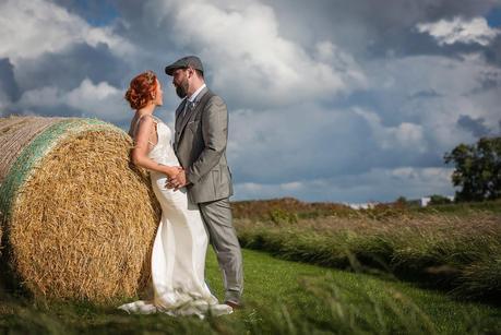 bride and groom leaning against hay bails 