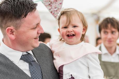 a little girl smiling with her father at a wedding 