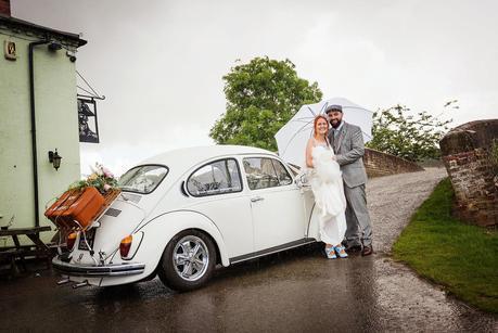 bride and groom in the rain by their wedding car