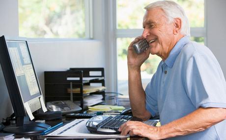 Man in home office on telephone using computer smiling