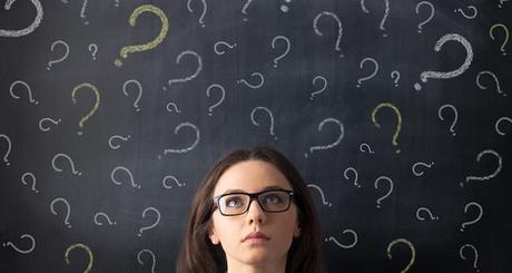 Chalk question marks above businesswoman at blackboard