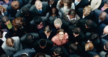 Businesswoman Looking up at Camera and Standing Outdoors Surrounded by a Large Group of Business People